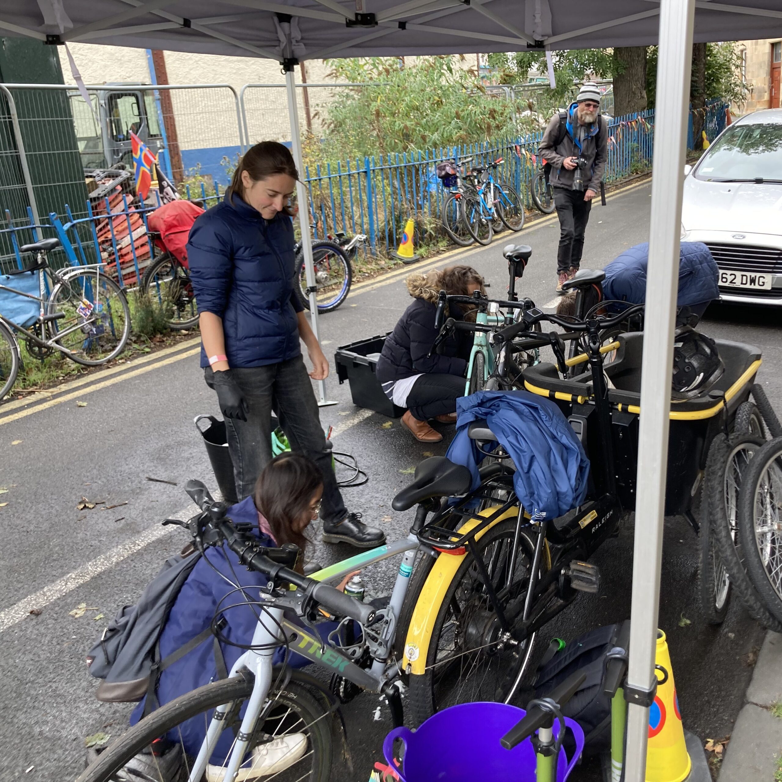 Volunteer assisting two workshop attendees at an outdoor cycle maintenance event.